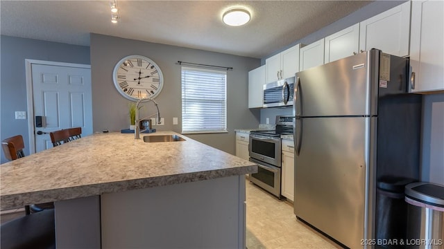 kitchen with appliances with stainless steel finishes, a sink, white cabinets, a breakfast bar area, and light countertops