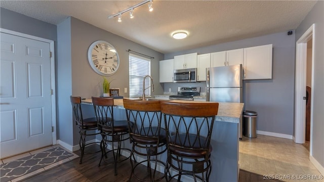 kitchen with appliances with stainless steel finishes, a kitchen breakfast bar, wood finished floors, track lighting, and baseboards