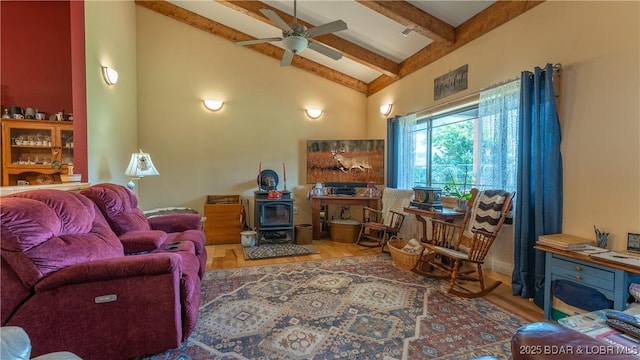 living area featuring ceiling fan, beamed ceiling, wood finished floors, a wood stove, and high vaulted ceiling