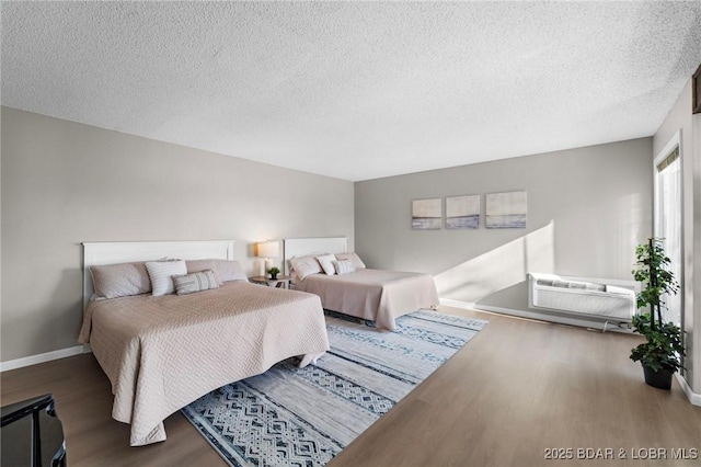 bedroom featuring a textured ceiling, a wall unit AC, wood finished floors, and baseboards