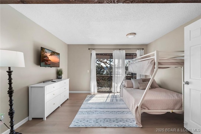 bedroom with a textured ceiling, access to outside, wood finished floors, and baseboards