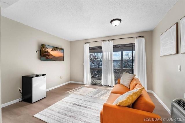 living area featuring a textured ceiling, wood finished floors, and baseboards