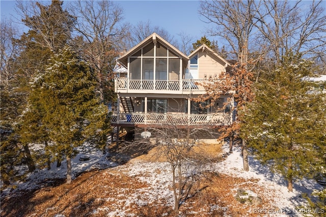 snow covered house featuring stairs and a sunroom