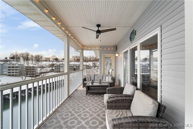 snow covered back of property featuring a water view, an outdoor living space, and a ceiling fan