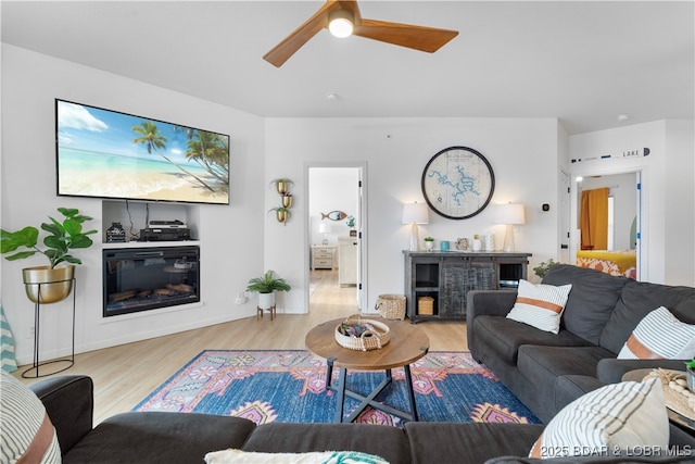 living room featuring light wood finished floors, ceiling fan, and a glass covered fireplace