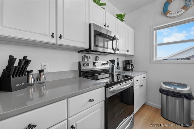 kitchen with appliances with stainless steel finishes, light wood-type flooring, white cabinetry, and baseboards