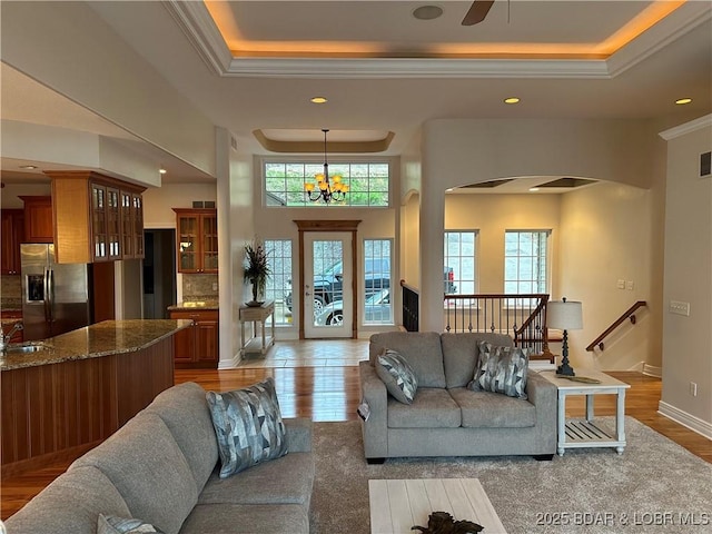 living room featuring a chandelier, a tray ceiling, light wood-style floors, and crown molding