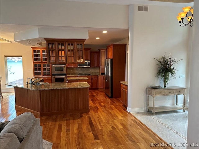 kitchen with stainless steel appliances, visible vents, glass insert cabinets, a sink, and wood finished floors