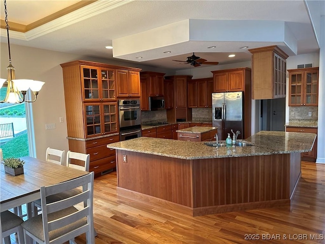 kitchen featuring a kitchen island with sink, a sink, hanging light fixtures, appliances with stainless steel finishes, and glass insert cabinets