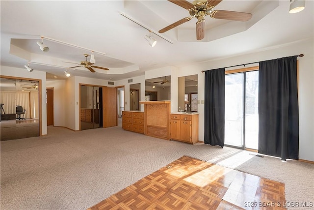 interior space featuring light colored carpet, a ceiling fan, access to outside, a tray ceiling, and rail lighting