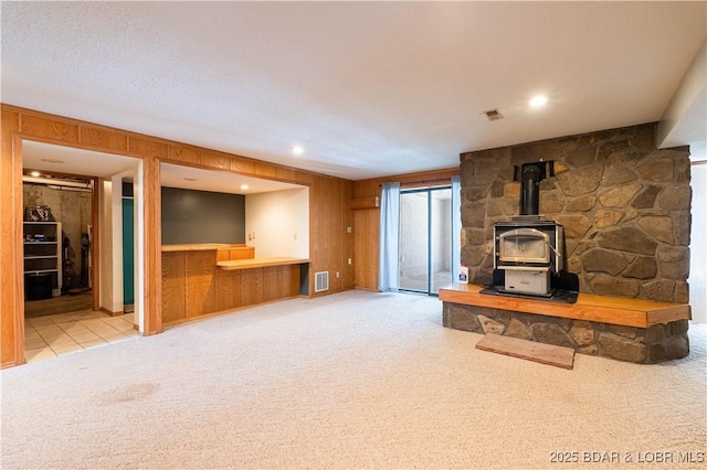 unfurnished living room with a wood stove, visible vents, wood walls, and carpet flooring