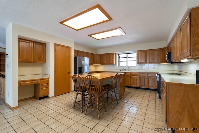 kitchen featuring decorative backsplash, butcher block countertops, stainless steel appliances, built in desk, and light tile patterned flooring