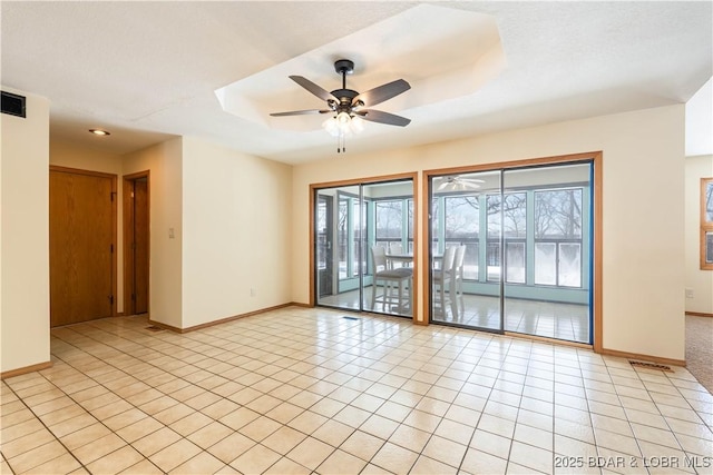 empty room featuring light tile patterned floors, a raised ceiling, visible vents, ceiling fan, and baseboards