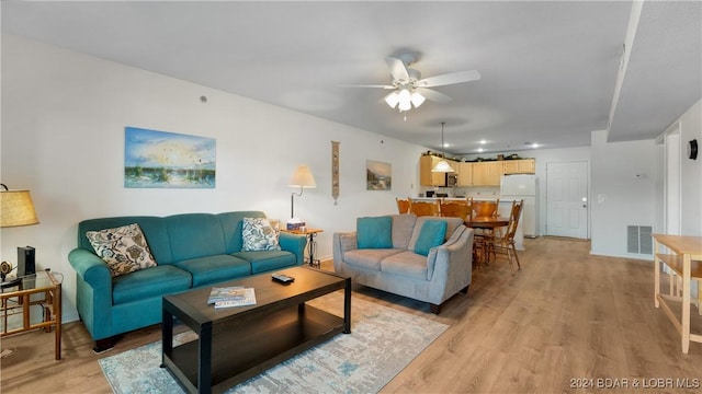 living room with light wood-style flooring, visible vents, ceiling fan, and baseboards