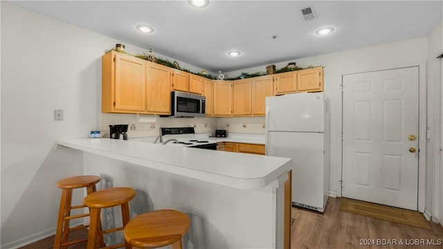 kitchen with light countertops, stainless steel microwave, electric range oven, light brown cabinetry, and freestanding refrigerator