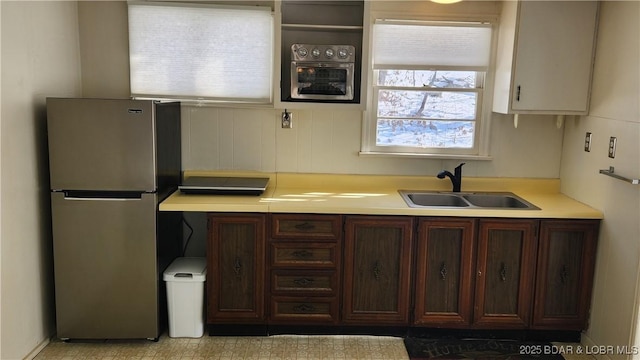 kitchen with freestanding refrigerator, light countertops, a sink, and dark brown cabinetry