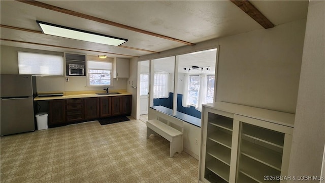 kitchen featuring dark brown cabinetry, beamed ceiling, freestanding refrigerator, light countertops, and a sink