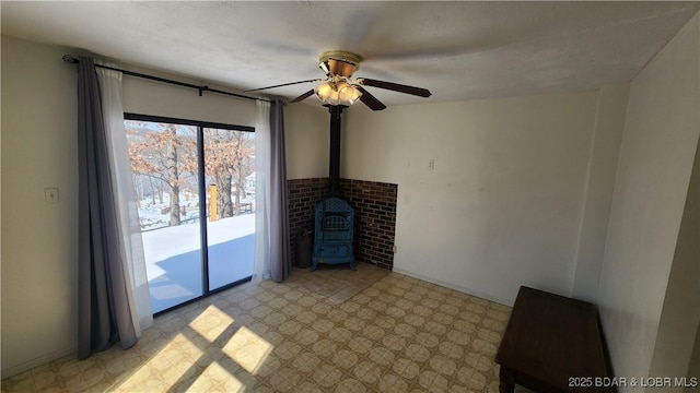 unfurnished living room featuring a wood stove, light floors, and a ceiling fan