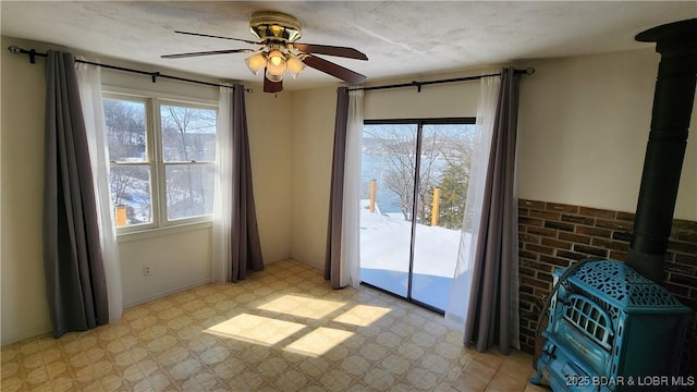 interior space with a wood stove, a healthy amount of sunlight, ceiling fan, and light floors