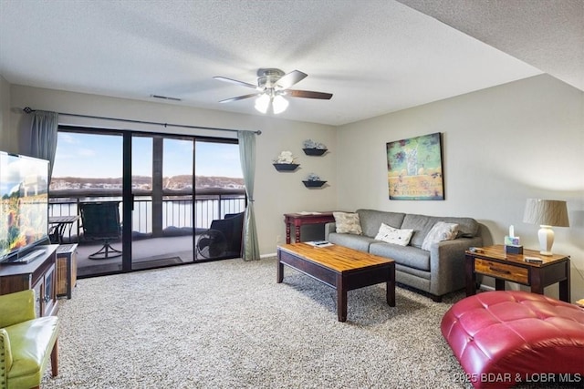 living area with carpet, a water view, visible vents, ceiling fan, and a textured ceiling