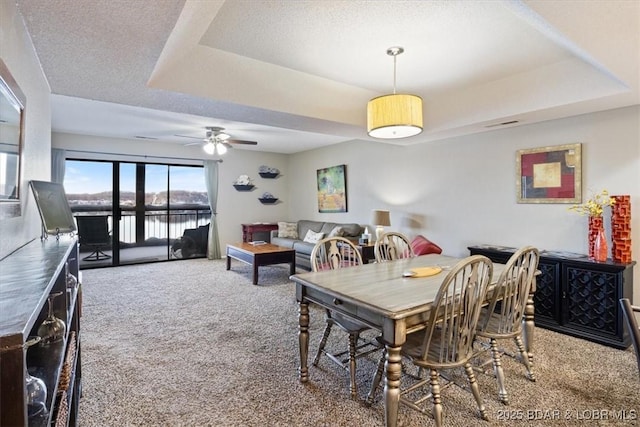 dining area featuring carpet flooring, a textured ceiling, ceiling fan, and a raised ceiling