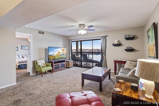 carpeted living area featuring a textured ceiling, baseboards, visible vents, and a ceiling fan