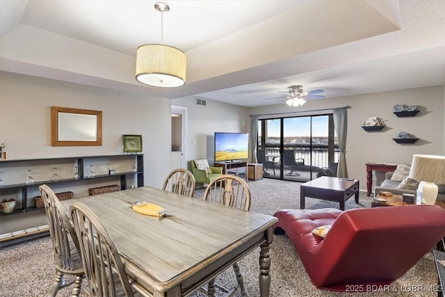 carpeted dining space with visible vents, a tray ceiling, and a ceiling fan