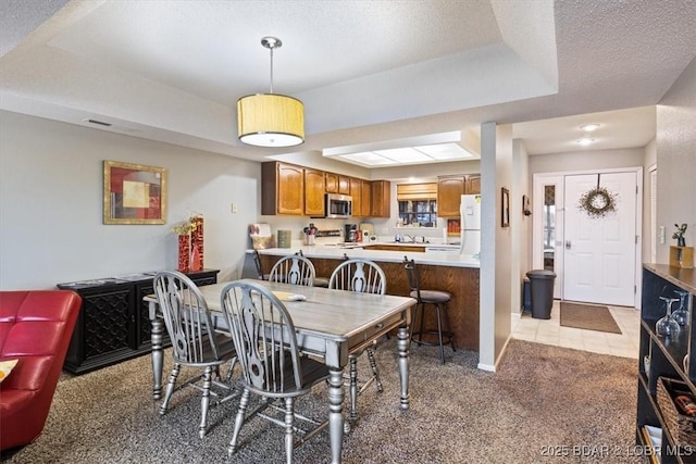 dining space featuring light carpet, a tray ceiling, and a textured ceiling