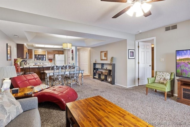 living area featuring a ceiling fan, visible vents, baseboards, light carpet, and a tray ceiling
