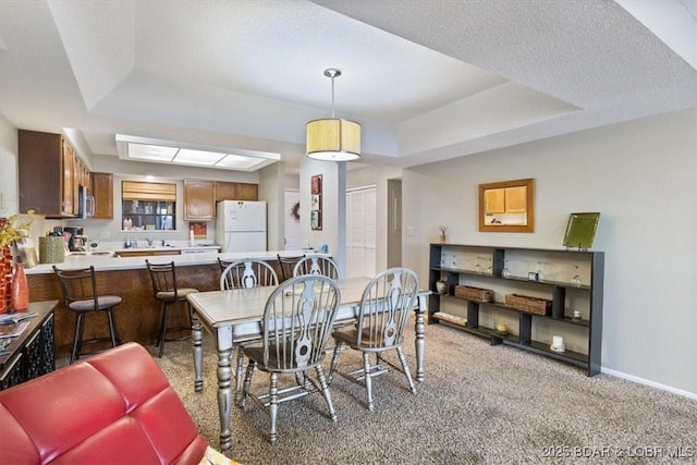 dining room featuring baseboards, a raised ceiling, and light carpet