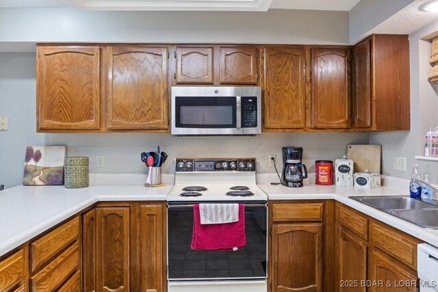 kitchen with brown cabinetry, electric range, stainless steel microwave, and light countertops