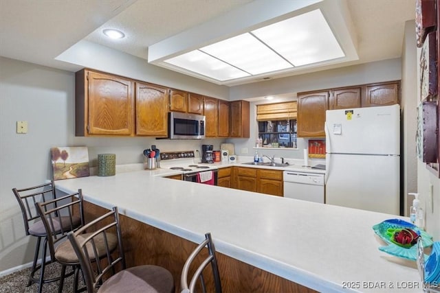 kitchen with white appliances, brown cabinets, a kitchen breakfast bar, a peninsula, and light countertops