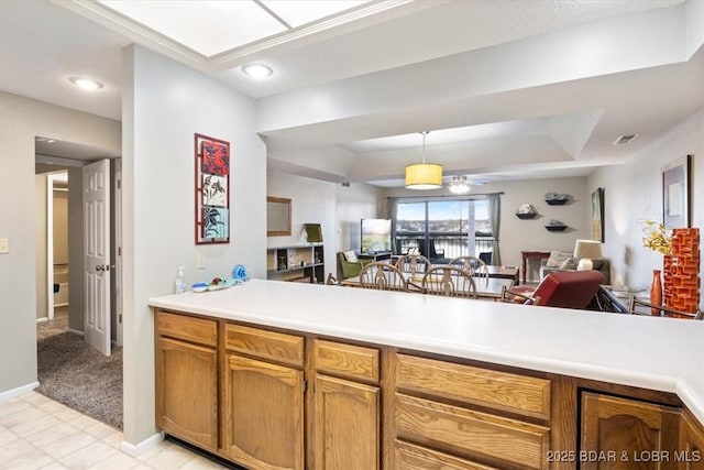 kitchen with a tray ceiling, brown cabinets, light countertops, visible vents, and open floor plan