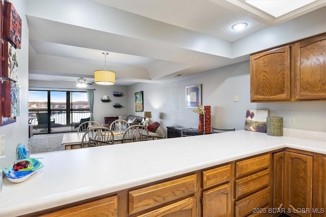 kitchen with hanging light fixtures, light countertops, brown cabinetry, a ceiling fan, and a tray ceiling