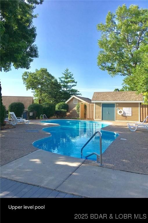 community pool with an outbuilding, an exterior structure, a patio area, and fence