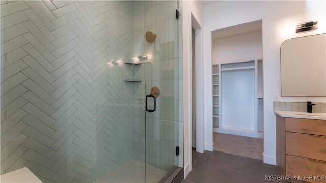 full bathroom featuring a spacious closet, a shower stall, vanity, and baseboards