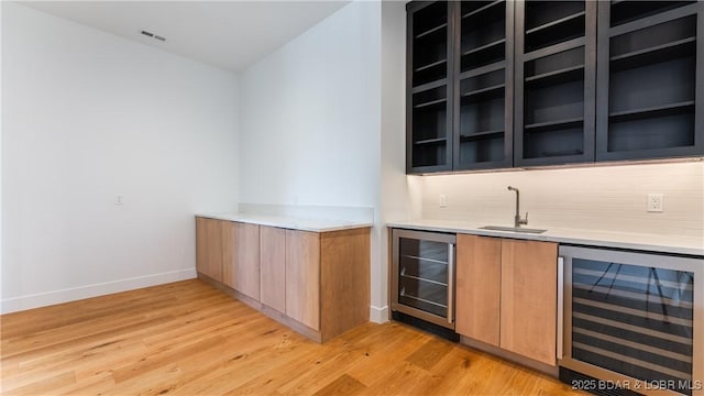 bar with wine cooler, a sink, light wood-style flooring, and decorative backsplash