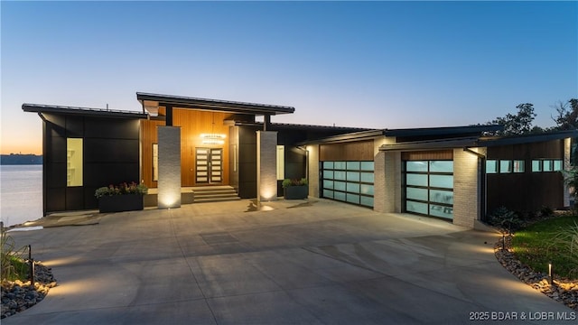 contemporary house with concrete driveway, brick siding, an attached garage, and a water view