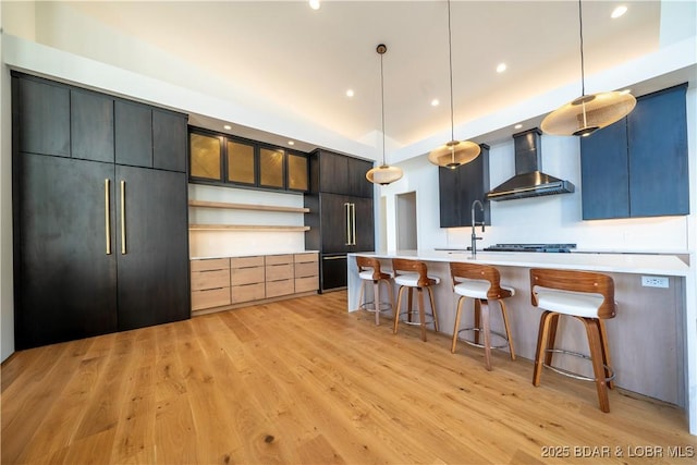 kitchen featuring light wood-style floors, pendant lighting, light countertops, and wall chimney exhaust hood