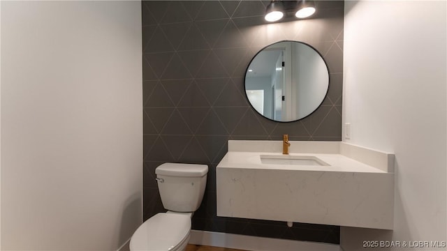 half bathroom with a sink, tile walls, and toilet