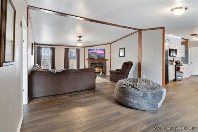 living room featuring vaulted ceiling, dark wood-style flooring, a fireplace, and ceiling fan