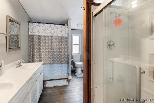 bathroom featuring double vanity, a shower, toilet, wood finished floors, and a sink