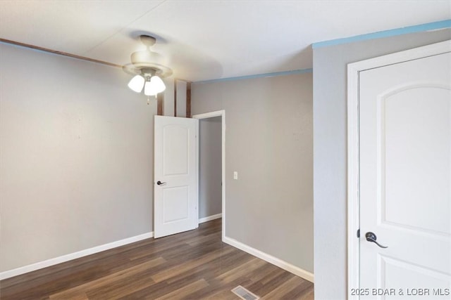 empty room featuring ceiling fan, dark wood finished floors, visible vents, and baseboards