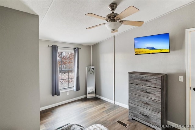 bedroom with light wood finished floors, visible vents, a ceiling fan, a textured ceiling, and baseboards