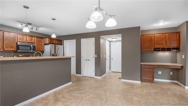 kitchen with appliances with stainless steel finishes, brown cabinetry, built in study area, and decorative light fixtures