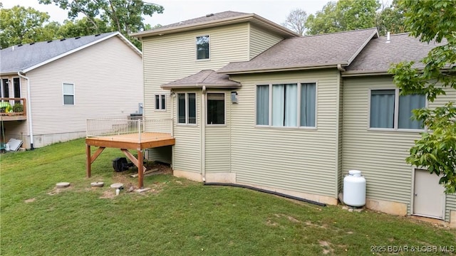 rear view of property with a wooden deck, roof with shingles, and a yard