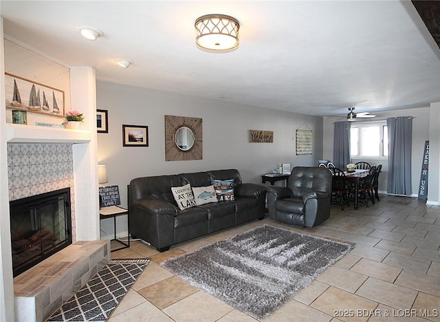 living room featuring a ceiling fan, a tile fireplace, light tile patterned flooring, and baseboards