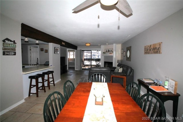 tiled dining space featuring a fireplace, baseboards, and ceiling fan