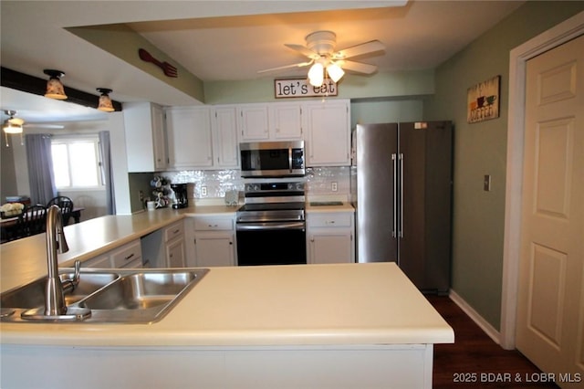 kitchen with light countertops, appliances with stainless steel finishes, white cabinets, a sink, and a peninsula