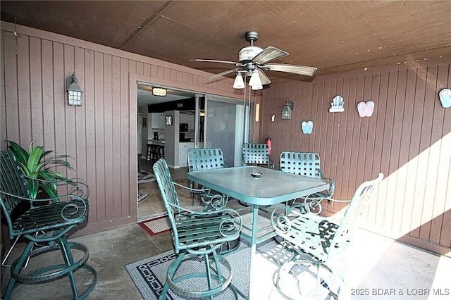 dining area featuring wood walls, ceiling fan, and concrete flooring